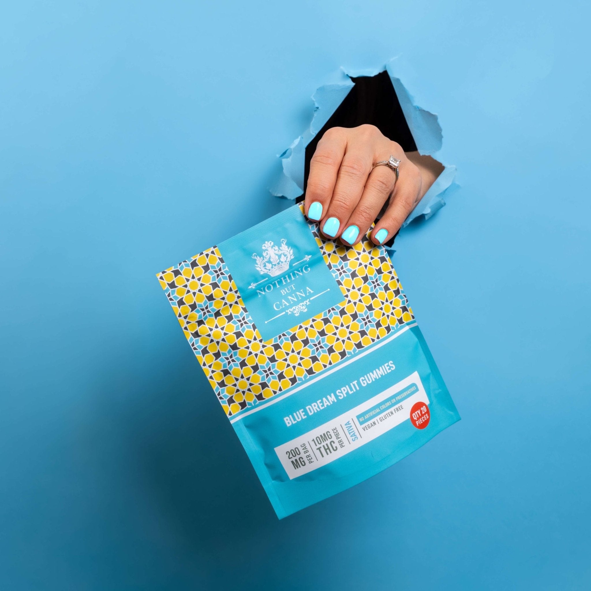 Hand with blue fingernails holding Nothing But Hemp Blue Dream hemp-derived delta-9 THC sativa gummies bag by the corner through a hole in a blue background